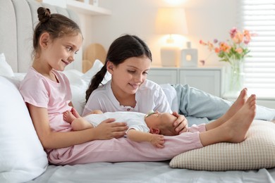 Photo of Big sisters with newborn baby on bed at home