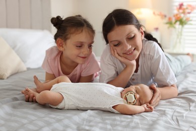 Photo of Big sisters admiring newborn baby on bed at home
