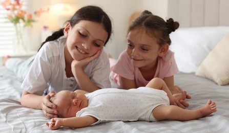 Photo of Big sisters admiring newborn baby on bed at home