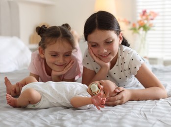 Photo of Big sisters admiring newborn baby on bed at home