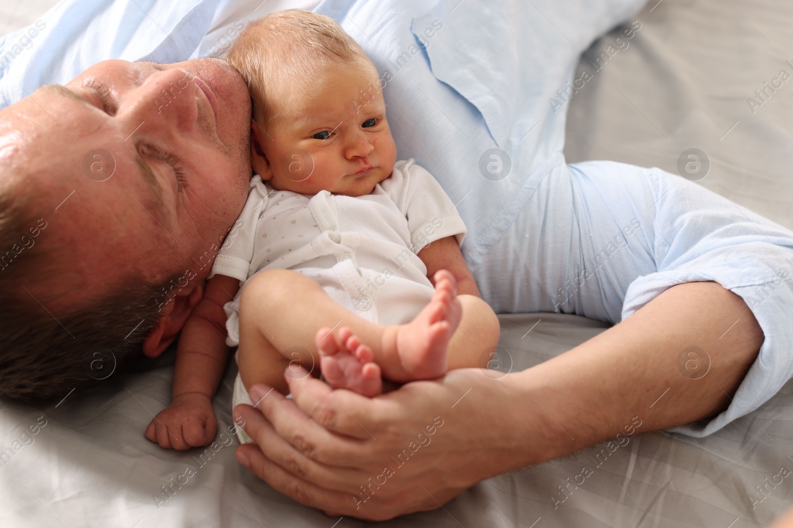 Father with his newborn baby lying on bed at home, closeup Photo of Father with his newborn baby lying on bed at home, closeup