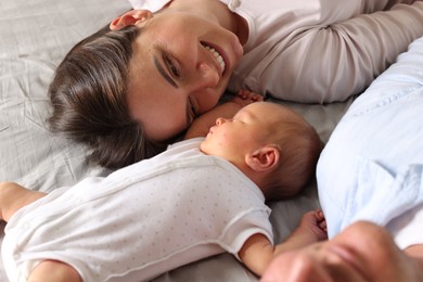Photo of Mother and father with their newborn baby lying on bed at home, closeup