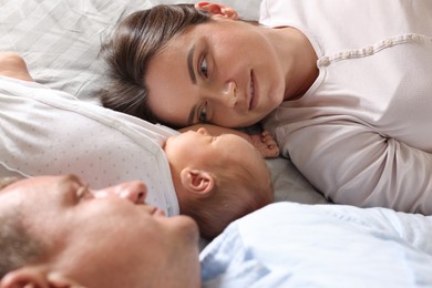 Photo of Mother and father with their newborn baby lying on bed at home, closeup