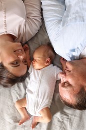 Photo of Mother and father with their newborn baby lying on bed at home, top view
