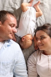 Photo of Mother and father with their newborn baby lying on bed at home, top view
