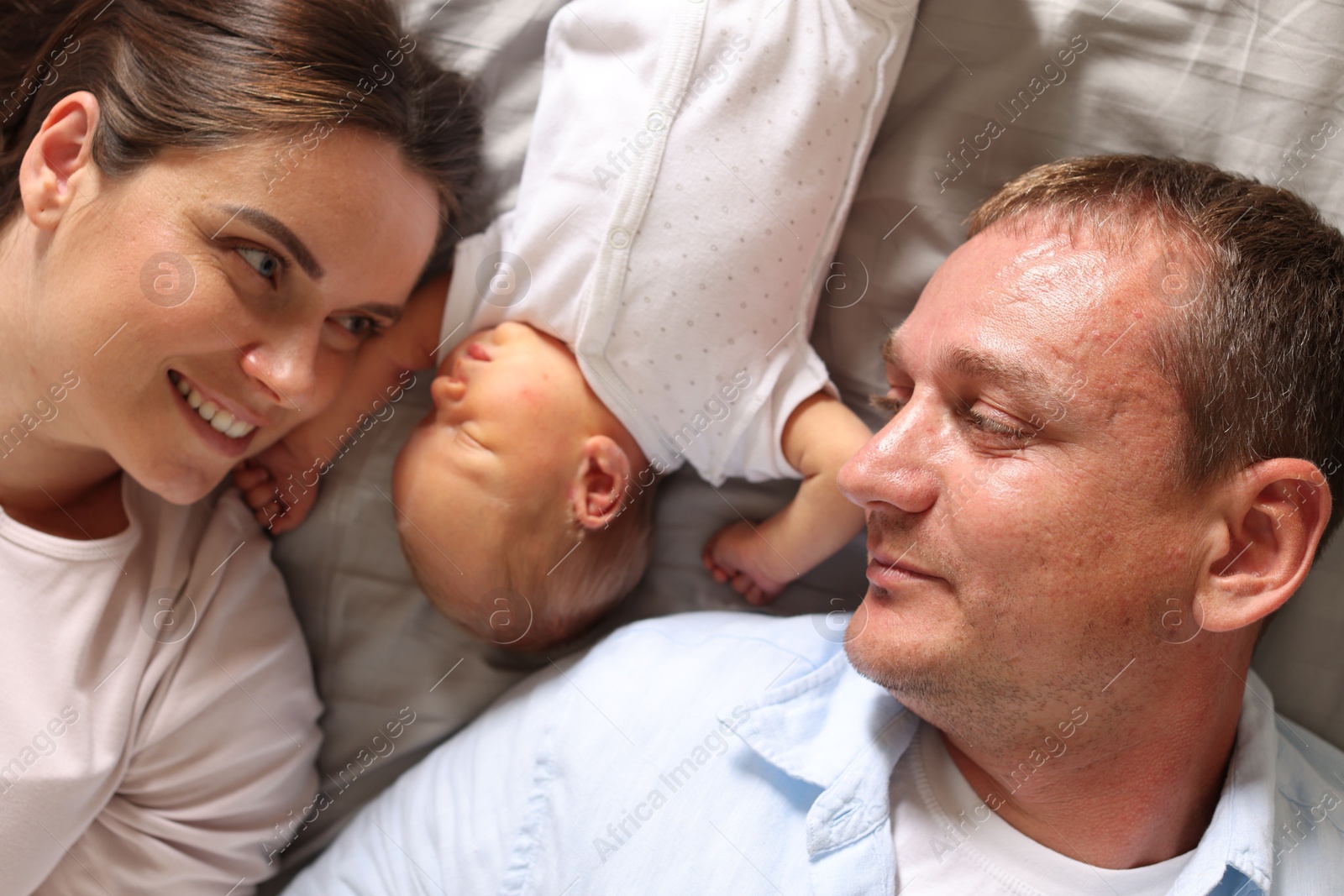 Mother and father with their newborn baby lying on bed at home, top view Photo of Mother and father with their newborn baby lying on bed at home, top view