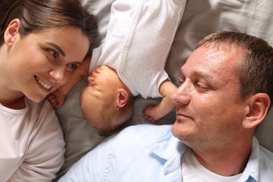 Photo of Mother and father with their newborn baby lying on bed at home, top view