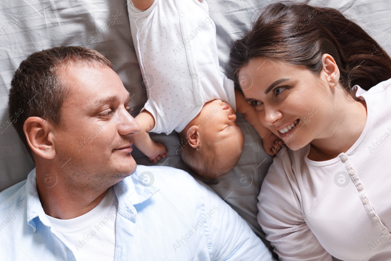 Mother and father with their newborn baby lying on bed at home, top view Photo of Mother and father with their newborn baby lying on bed at home, top view