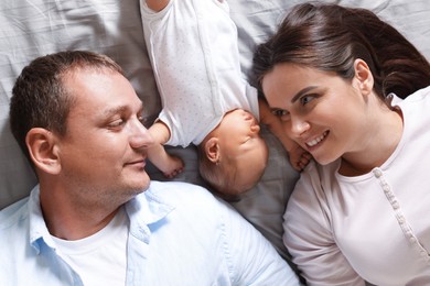 Photo of Mother and father with their newborn baby lying on bed at home, top view
