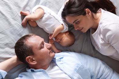Photo of Mother and father with their newborn baby lying on bed at home, top view