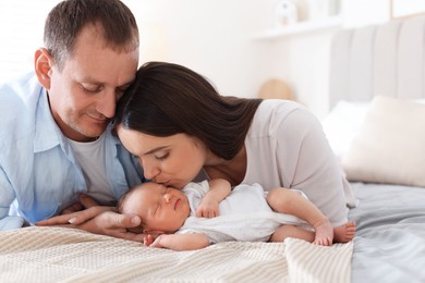 Photo of Mom and dad with their newborn baby on bed at home