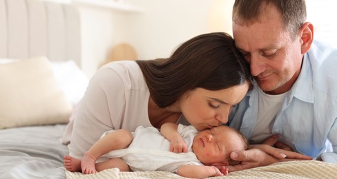 Photo of Mom and dad with their newborn baby on bed at home
