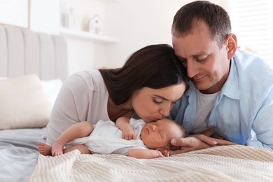 Photo of Mom and dad with their newborn baby on bed at home