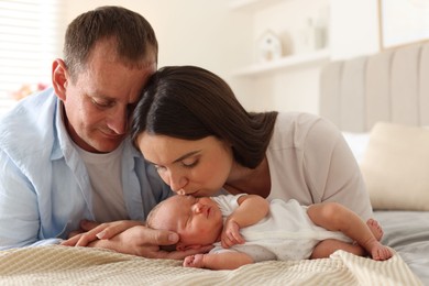 Photo of Mom and dad with their newborn baby on bed at home