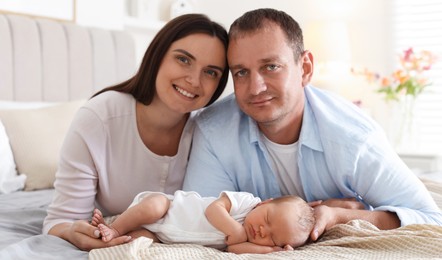 Photo of Mom and dad with their newborn baby on bed at home