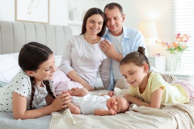 Photo of Parents watching their older daughters admiring newborn baby on bed at home, selective focus