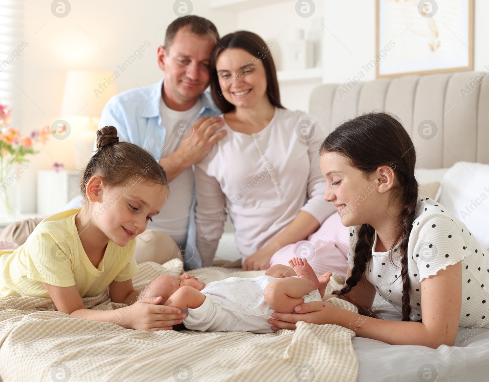 Photo of Parents watching their older daughters admiring newborn baby on bed at home, selective focus