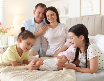 Photo of Parents watching their older daughters admiring newborn baby on bed at home, selective focus