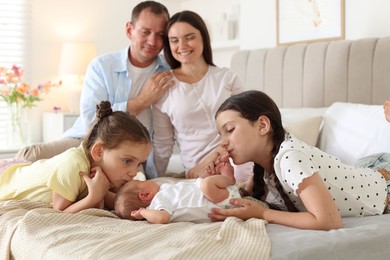 Photo of Parents watching their older daughters admiring newborn baby on bed at home, selective focus
