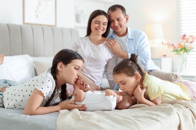 Photo of Parents watching their older daughters admiring newborn baby on bed at home, selective focus