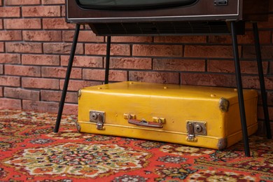 Photo of Retro TV on stand, suitcase and carpet near red brick wall, closeup. Used stuff