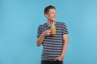 Photo of Happy man with mason jar of orange juice on light blue background. Refreshing drink