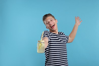 Photo of Happy man with mason jar of lemonade on light blue background. Refreshing drink
