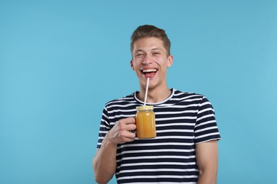 Photo of Happy man with mason jar of orange juice on light blue background. Refreshing drink