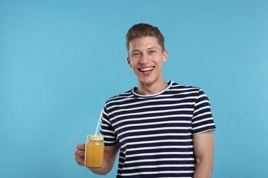 Photo of Happy man with mason jar of orange juice on light blue background. Refreshing drink
