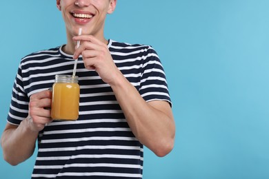 Photo of Happy man with mason jar of orange juice on light blue background, closeup with space for text. Refreshing drink