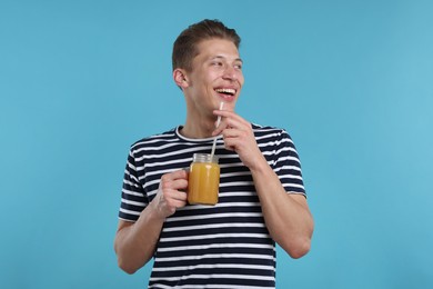 Photo of Happy man with mason jar of orange juice on light blue background. Refreshing drink