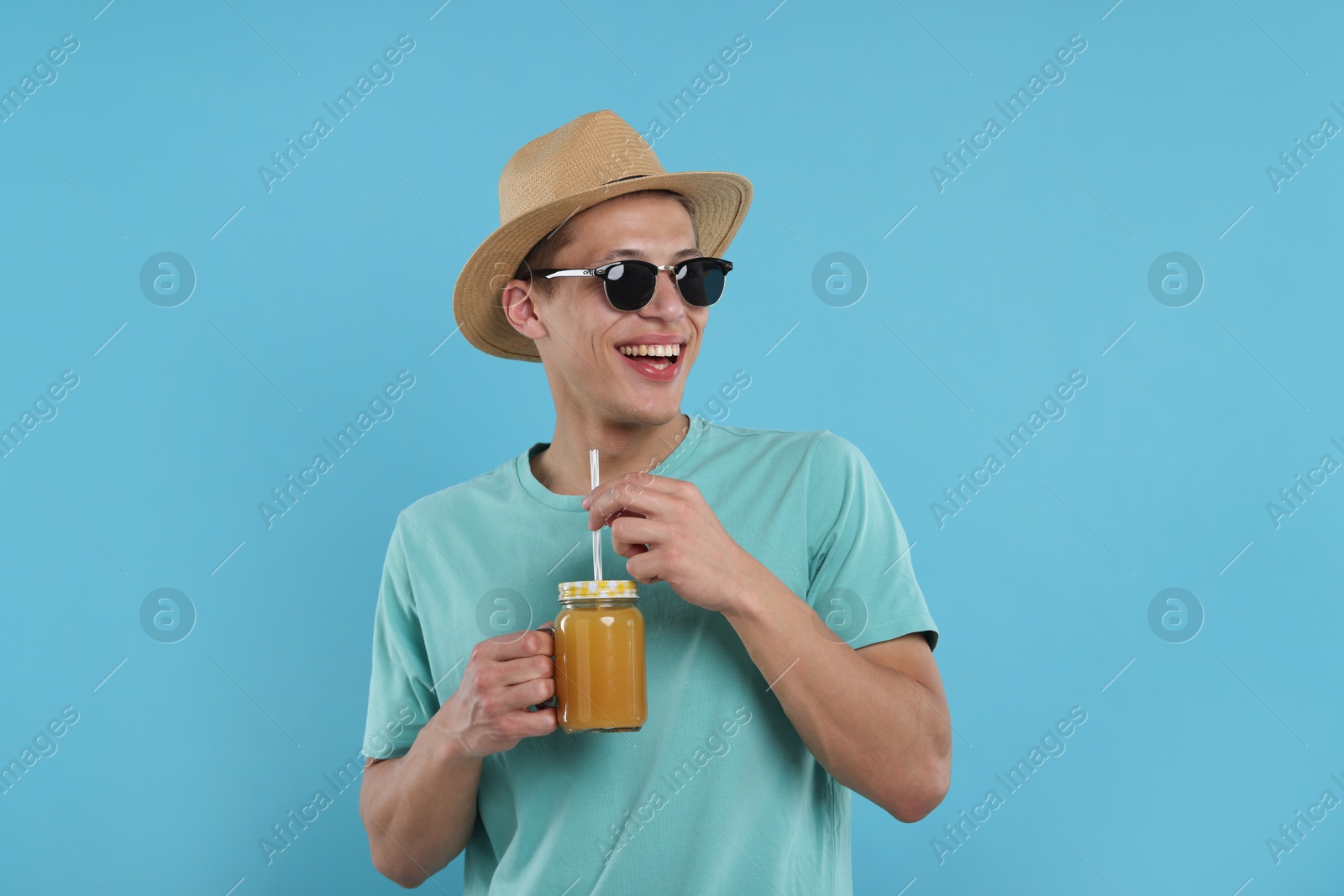 Happy man in sunglasses and hat with mason jar of orange juice on light blue background. Refreshing drink Photo of Happy man in sunglasses and hat with mason jar of orange juice on light blue background. Refreshing drink