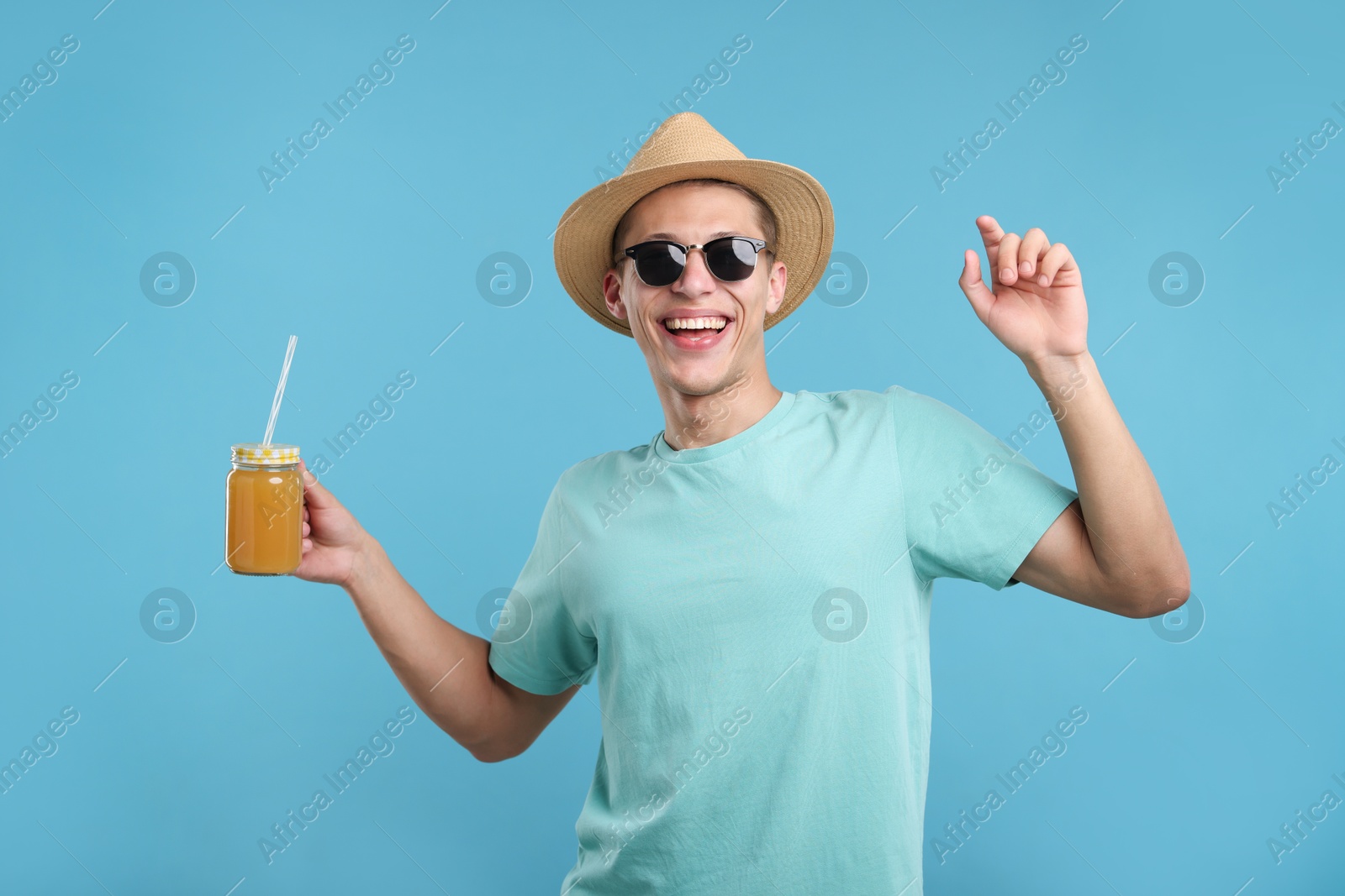 Happy man in sunglasses and hat with mason jar of orange juice on light blue background. Refreshing drink Photo of Happy man in sunglasses and hat with mason jar of orange juice on light blue background. Refreshing drink