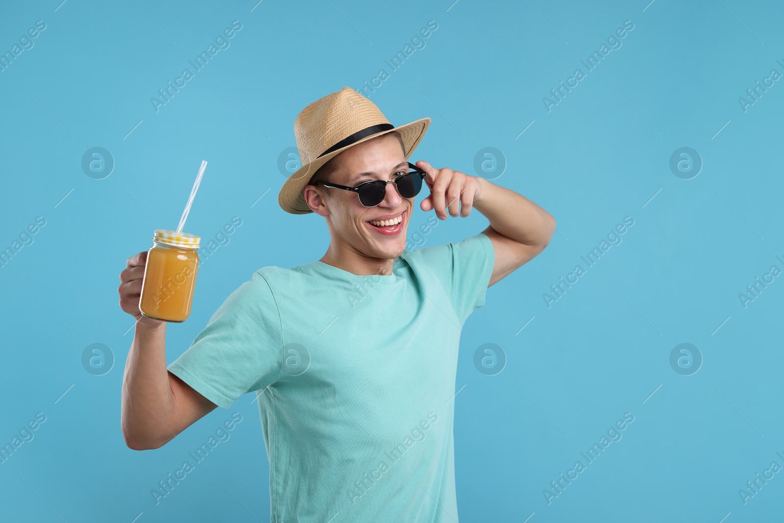 Happy man in sunglasses and hat with mason jar of orange juice on light blue background. Refreshing drink Photo of Happy man in sunglasses and hat with mason jar of orange juice on light blue background. Refreshing drink