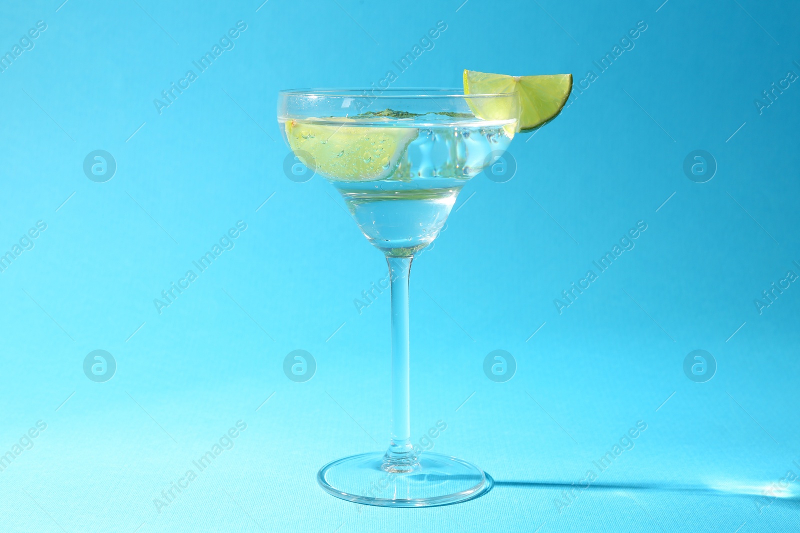 Martini cocktail with slices of lime and mint on light blue background Photo of Martini cocktail with slices of lime and mint on light blue background