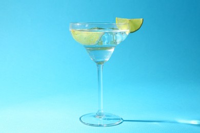 Photo of Martini cocktail with slices of lime and mint on light blue background