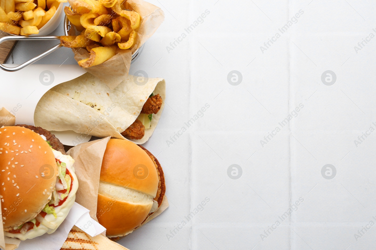 Different delicious fast food on white tiled table, flat lay. Space for text Photo of Different delicious fast food on white tiled table, flat lay. Space for text