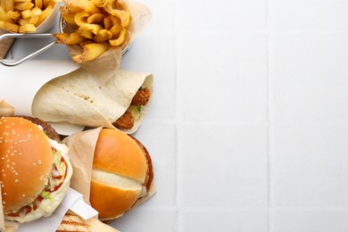 Photo of Different delicious fast food on white tiled table, flat lay. Space for text