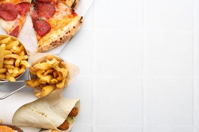 Photo of Different delicious fast food on white tiled table, flat lay. Space for text