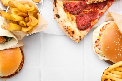 Photo of Different delicious fast food on white tiled table, flat lay. Space for text
