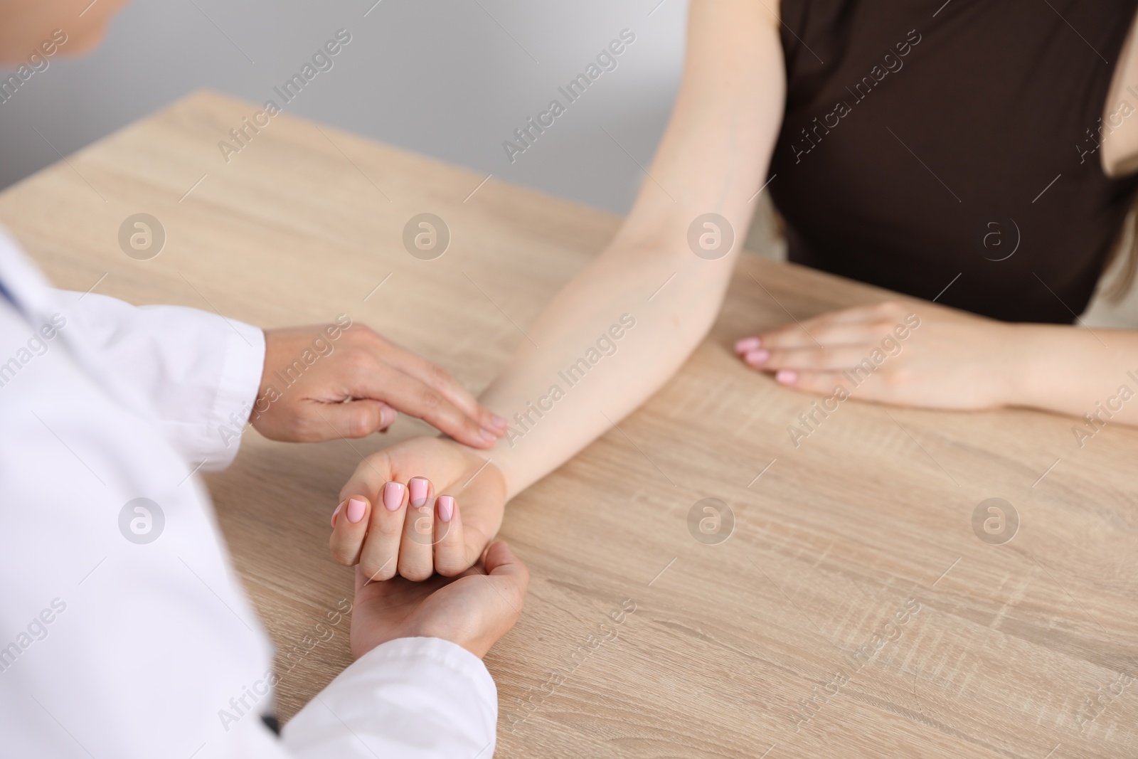 Photo of Doctor checking woman's pulse with fingers at wooden table indoors, closeup