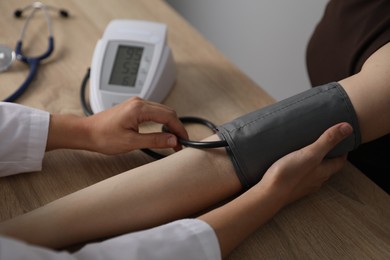 Photo of Doctor checking woman's heart rate and blood pressure via sphygmomanometer at wooden table indoors, closeup
