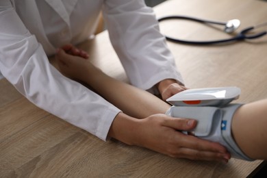Photo of Doctor checking woman's heart rate and blood pressure via sphygmomanometer at wooden table indoors, closeup