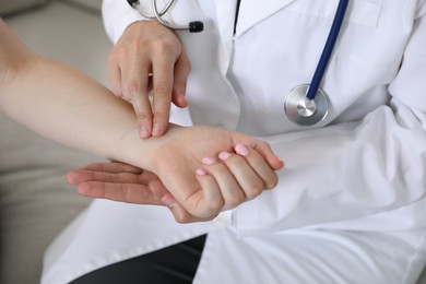 Photo of Doctor checking woman's pulse with fingers indoors, closeup