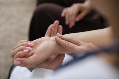 Photo of Doctor checking woman's pulse with fingers indoors, closeup