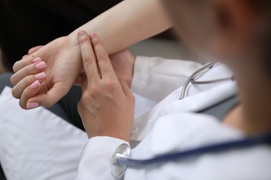 Photo of Doctor checking woman's pulse with fingers indoors, closeup