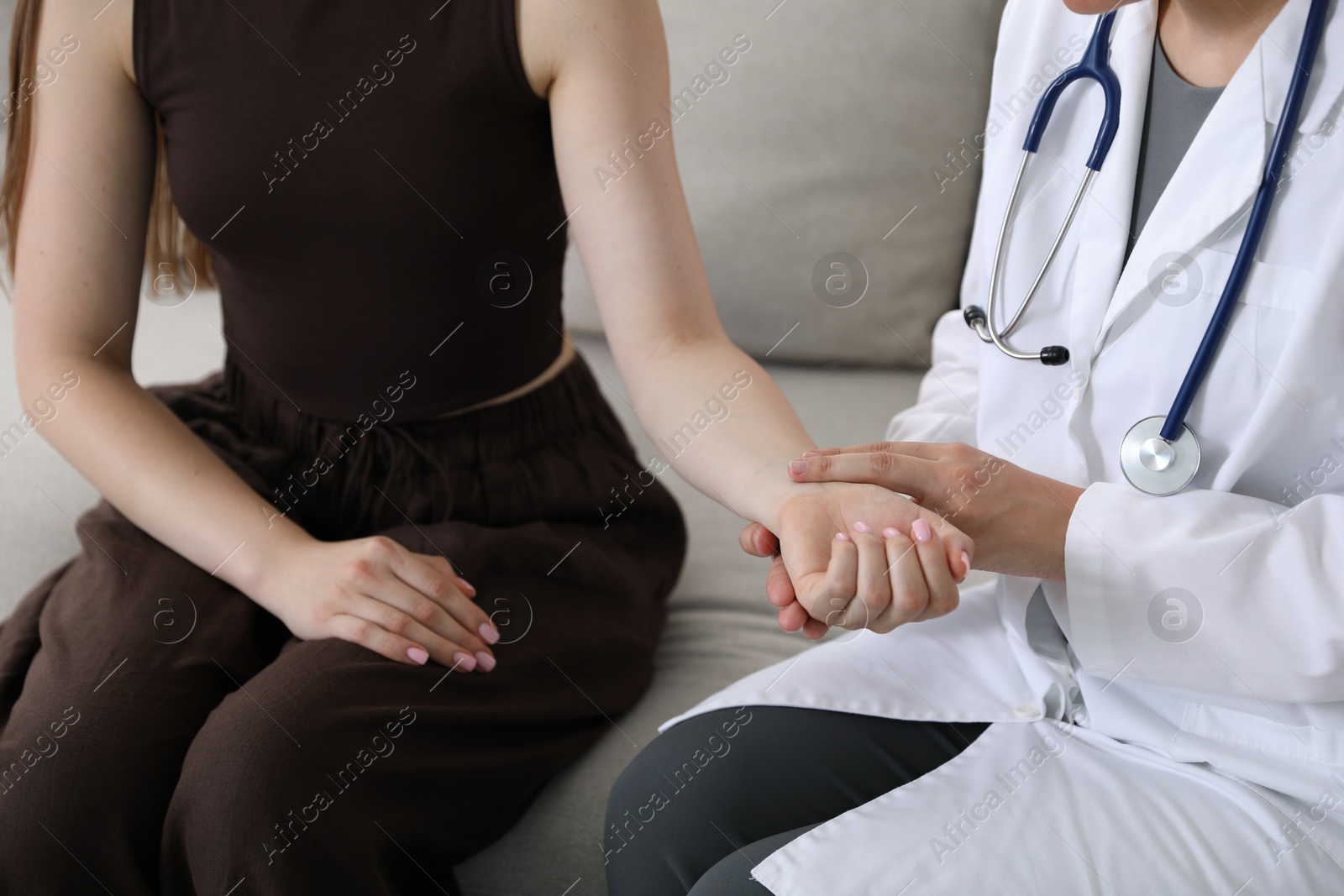 Photo of Doctor checking woman's pulse with fingers on sofa indoors, closeup