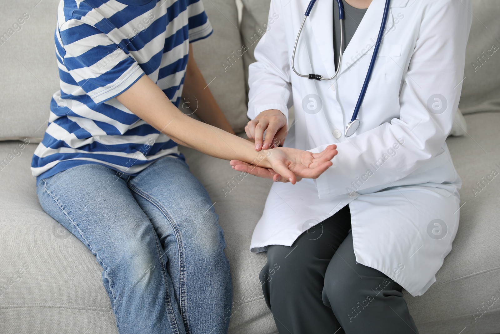 Photo of Doctor checking woman's pulse with fingers on sofa indoors, closeup