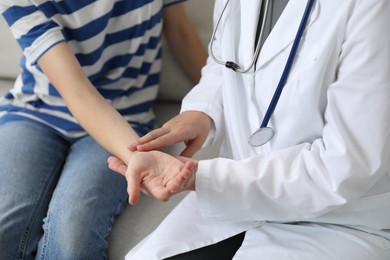 Photo of Doctor checking woman's pulse with fingers on sofa indoors, closeup