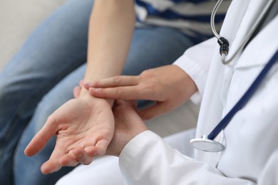 Photo of Doctor checking woman's pulse with fingers on sofa indoors, closeup